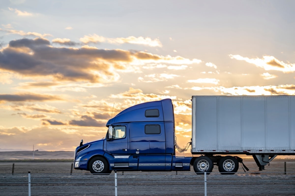 truck driving along road at sunset